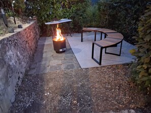 Un espacio de patio con un pozo de fuego, asientos y un muro de piedra.