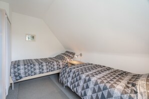 A small, triangular room with two beds, a nightstand, a lamp, and a framed picture on the wall.