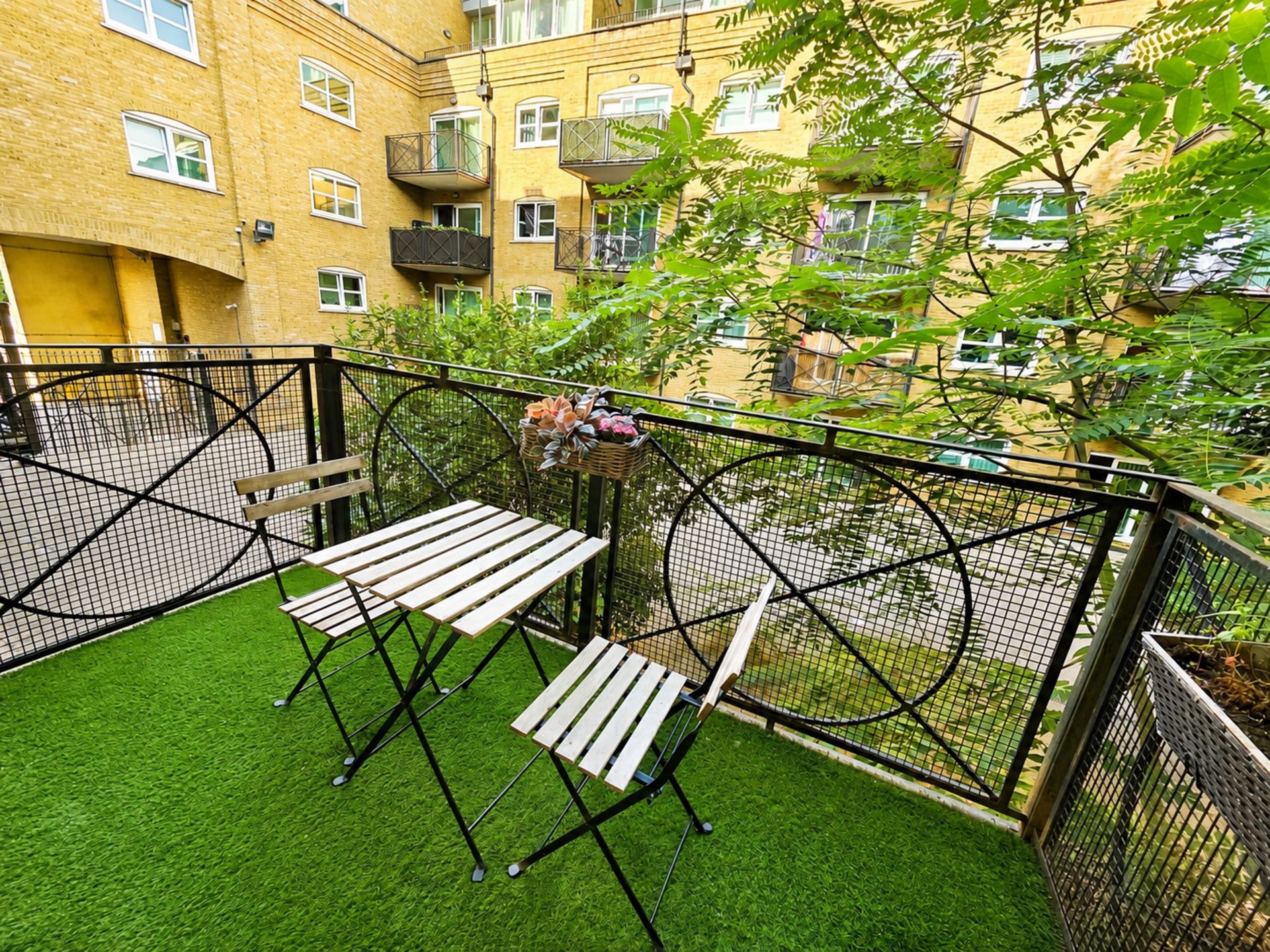 An outdoor balcony with artificial grass, metal fencing, and a table with benches.