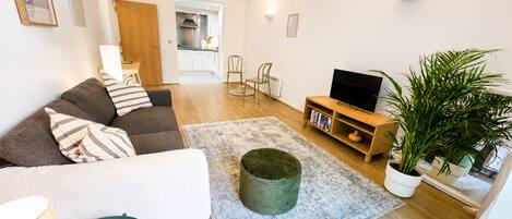 Una sala de estar con un sofá, una mesita de centro, un mueble para televisión y una planta en maceta.