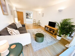 A living room with a sofa, a coffee table, a TV stand, and a potted plant. - Stylish Balcony Apartment, Walk to ExCeL & DLR (London)