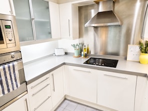 A modern kitchen with stainless steel appliances, white cabinetry, and a built-in oven. - Stylish Balcony Apartment, Walk to ExCeL & DLR (London)