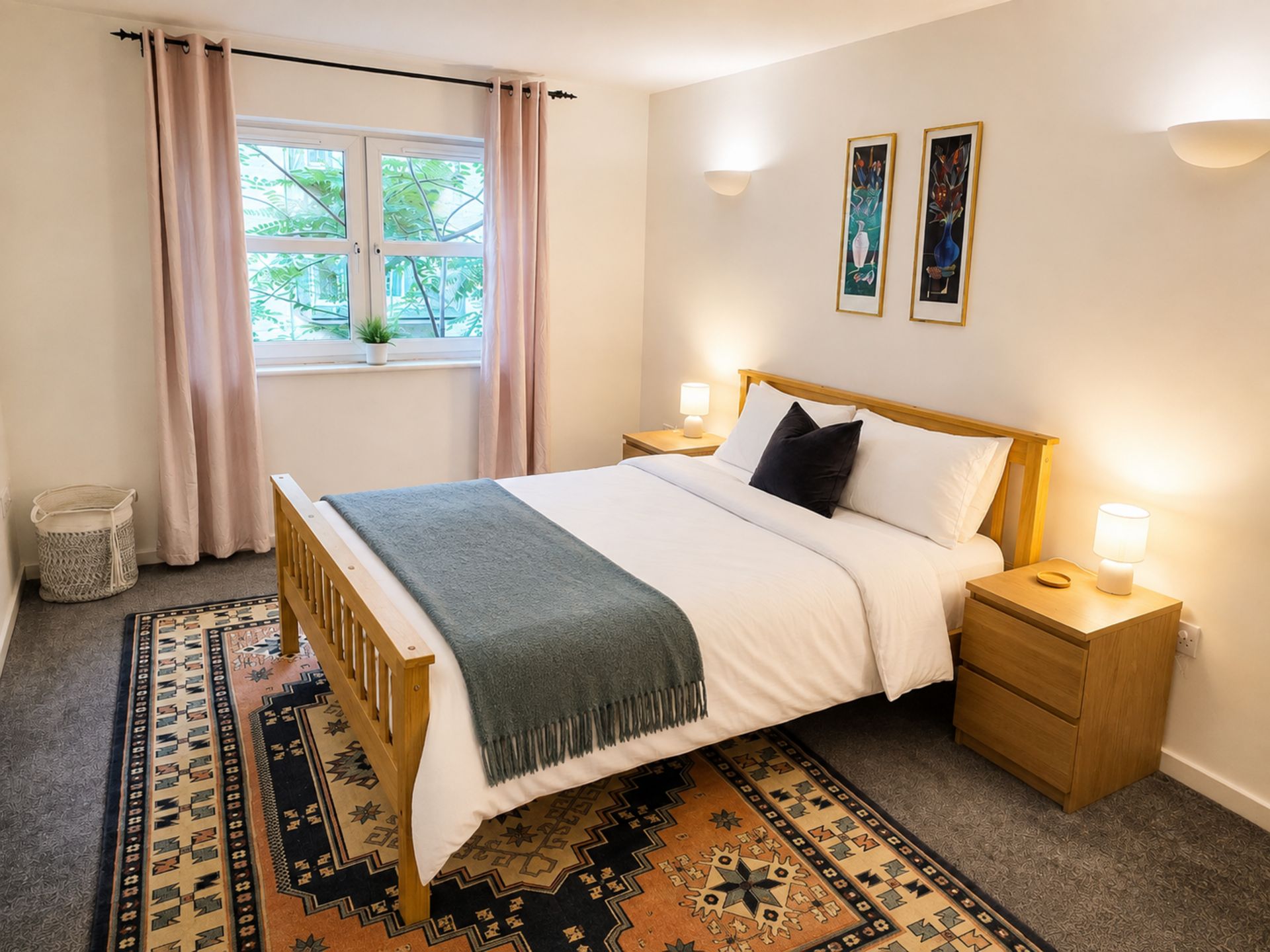 A bedroom with a bed, bedside tables, a window with curtains, a wall-mounted light fixture, and a rug.