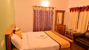 Una habitación de hotel con una cama, cabecera de madera, mesita de noche, lámpara, espejo, ventana con cortinas y un sillón de cuero.