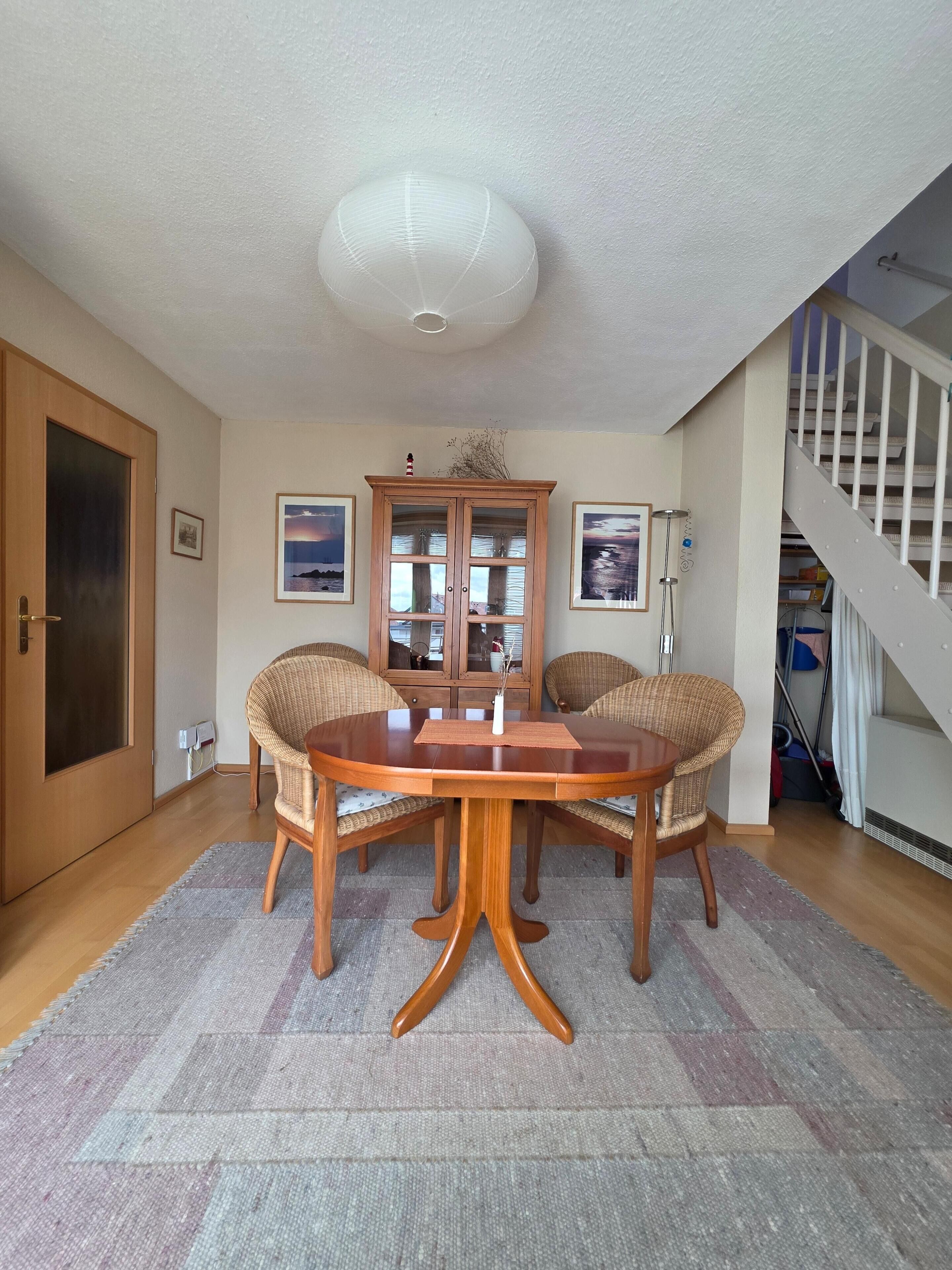 A dining area with a round wooden table, wicker chairs, and a cabinet with glass doors.