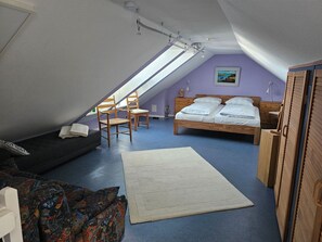Ein Schlafzimmer mit schrägen Wänden, einem Bett, einem Sessel, einem kleinen Tisch und einem Gemälde an der Wand.