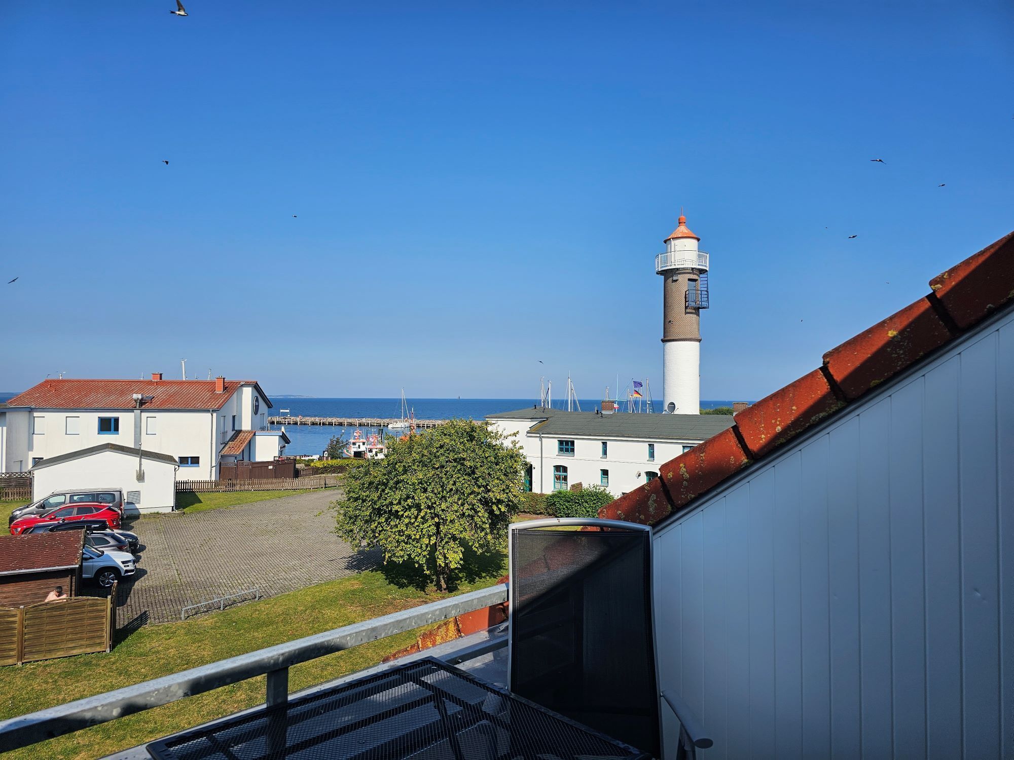 A coastal view with a lighthouse, buildings, and parked cars.