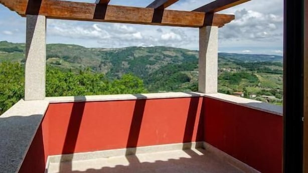 Un balcon avec vue sur des collines verdoyantes et un ciel dégagé.