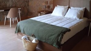 Une chambre avec un mur en pierre, un lit recouvert d’une couverture verte, une table de chevet et une chaise.