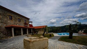Un bâtiment en pierre avec un toit rouge, une piscine et un banc en pierre au premier plan.