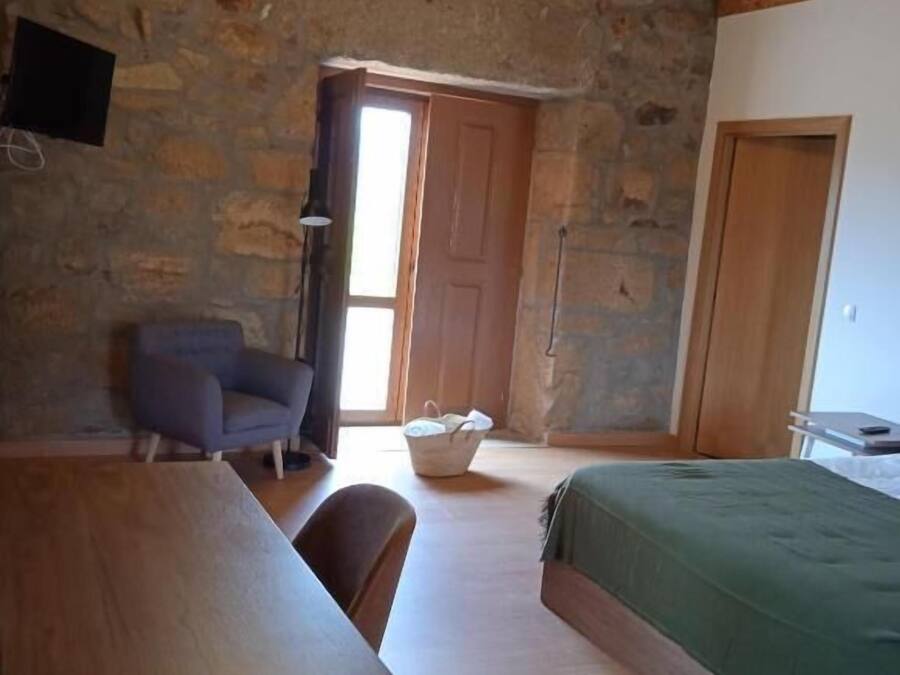 Una habitación con una mesa de madera, una silla, una cama con cubrecama verde y una pared de piedra.