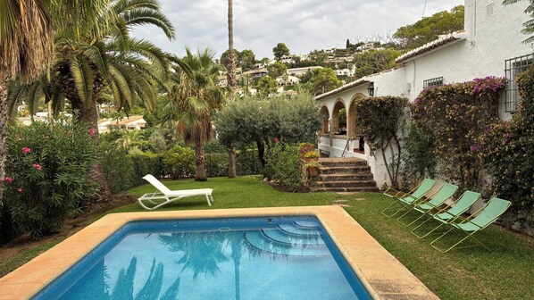 Una piscina con una zona verdeggiante, palme e un edificio bianco con archi.