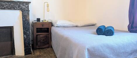 A bedroom with a bed, a nightstand, a lamp, a fireplace, and a window with curtains.