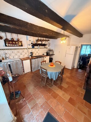 A kitchen with a round table, wooden chairs, and a tiled floor. - La Glycine, bastide du XIIIe (Montjoi)