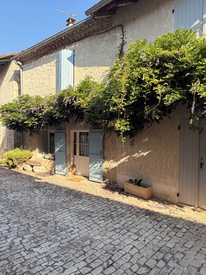 A building with a stone facade, a cobblestone courtyard, and a door with a blue shutter. - La Glycine, bastide du XIIIe (Montjoi)