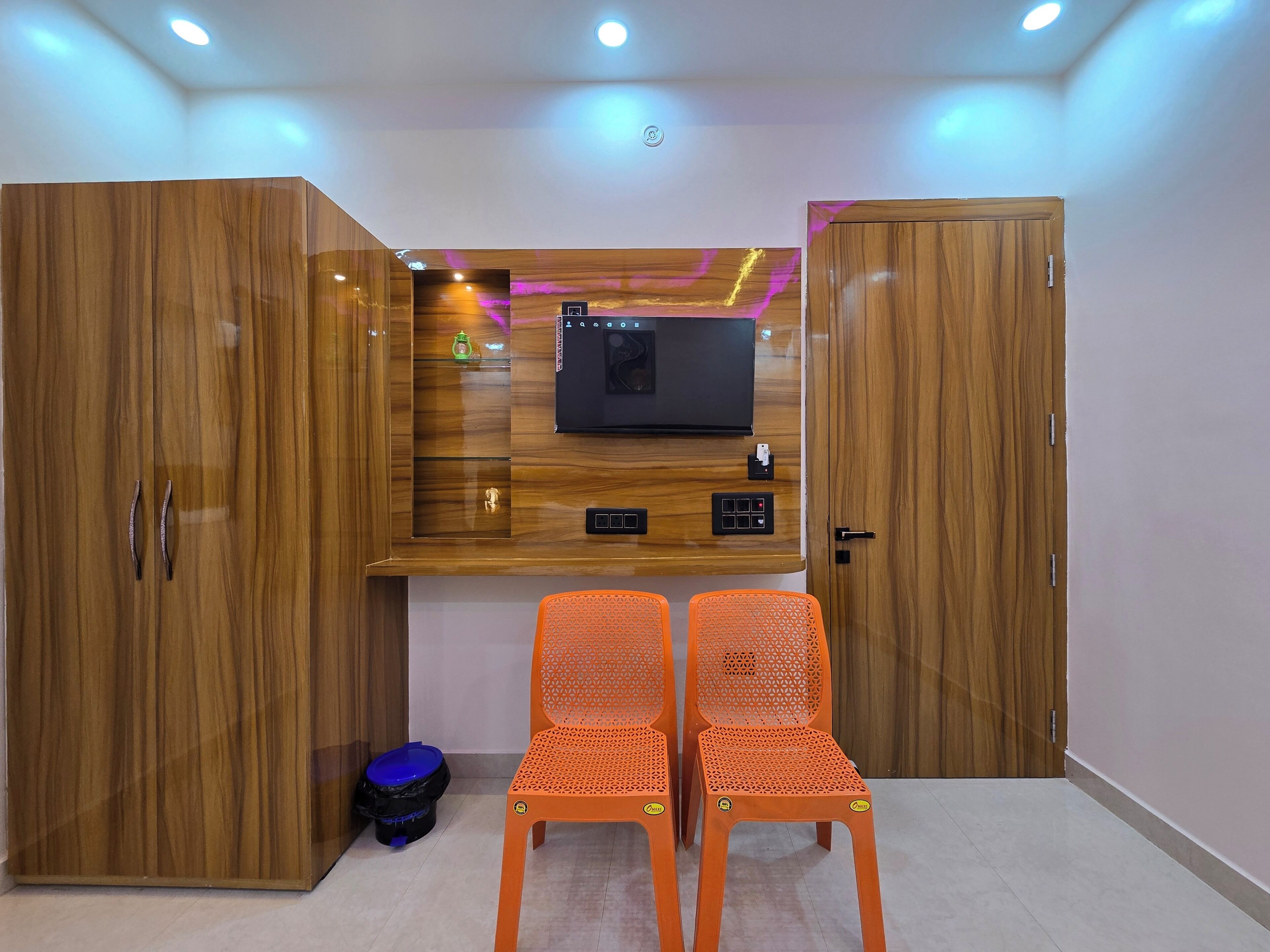 Una habitación con una estantería para televisor, dos sillas naranjas y armarios de madera.
