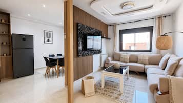 Ein modernes Wohnzimmer mit einer Couch, einem Couchtisch, einem an der Wand montierten Fernseher und einem Essbereich mit Stühlen und einem Tisch.