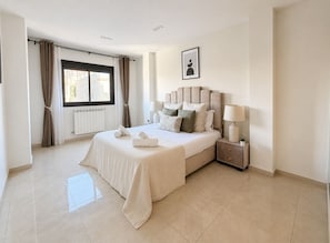 A modern bedroom with a large bed, a bedside table with a lamp, and a window with curtains.
