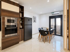 Una cocina moderna con electrodomésticos integrados, un comedor con mesa y sillas, y un ventanal corredizo que da a un espacio exterior.