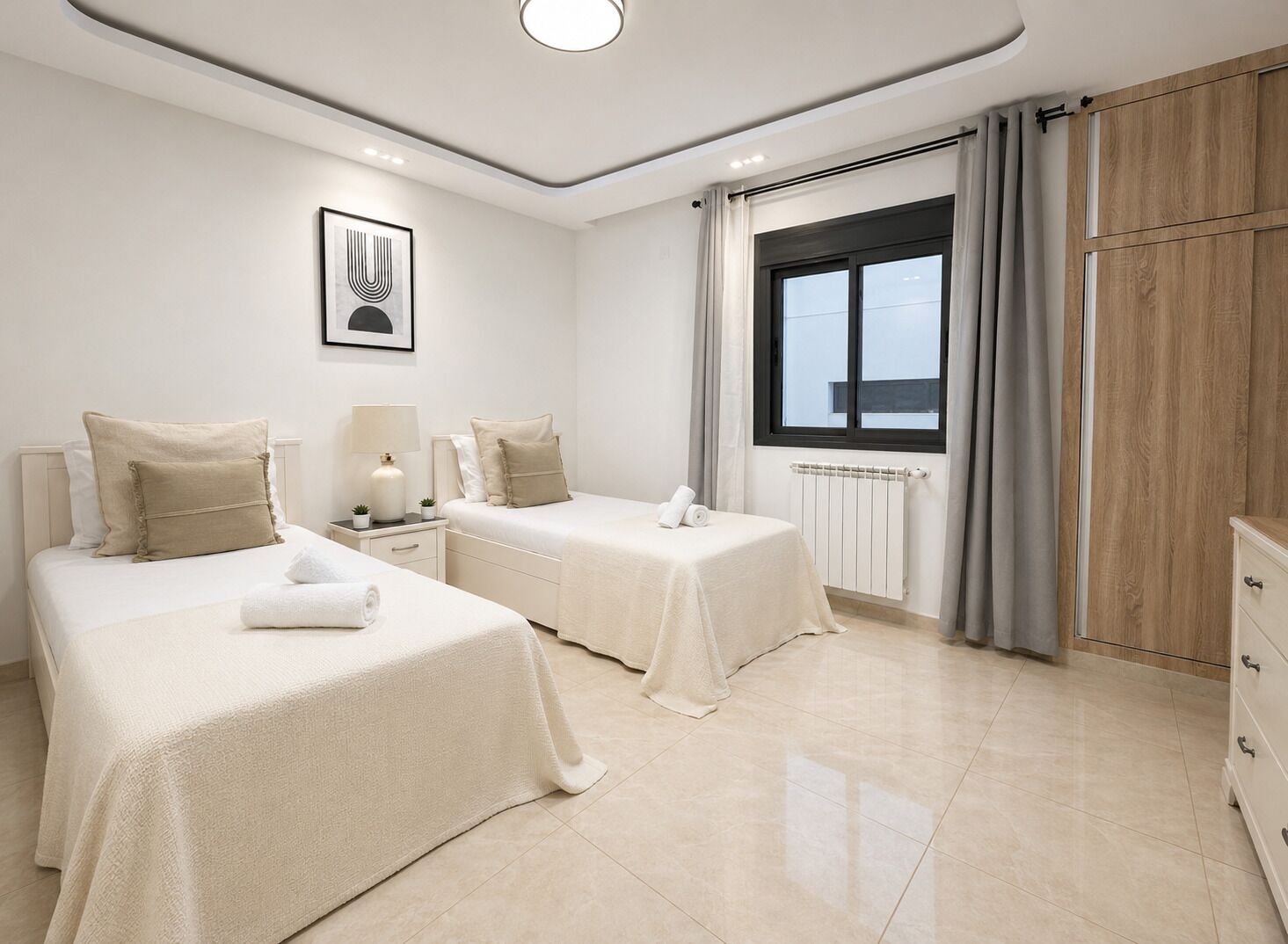 Una camera d'albergo con due letti, una finestra con tende, un termosifone e un armadio in legno.