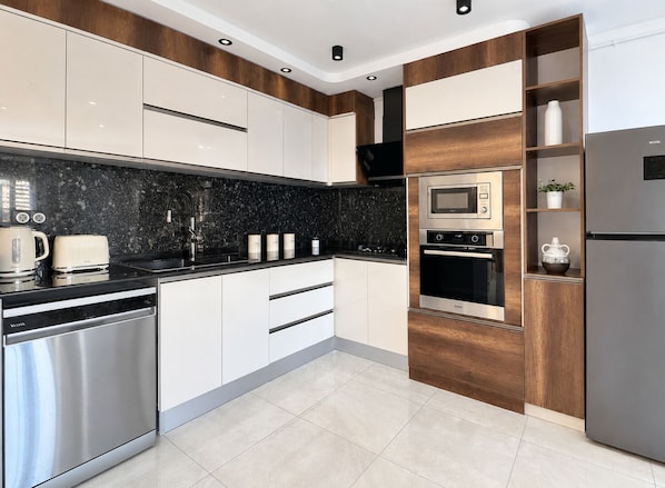 A modern kitchen with stainless steel appliances, a black granite countertop, and wooden cabinetry.