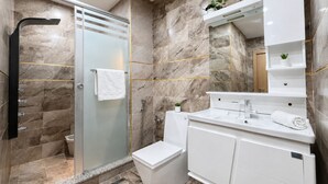 Ett modernt badrum med en dusch som är avskärmad med glasväggar, en vit toalett och en tvättställsmöbel med spegel.