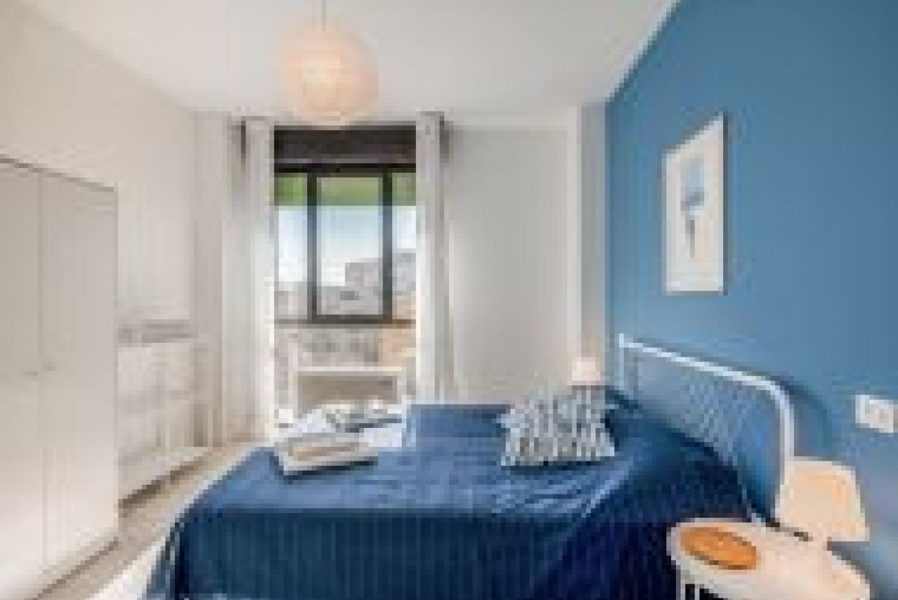 Un dormitorio con cama, mesita de noche, ventana y vista a la ciudad.