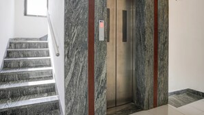 A marble staircase leading to an elevator with a digital display. - Collection O Shirdi (Shirdi)