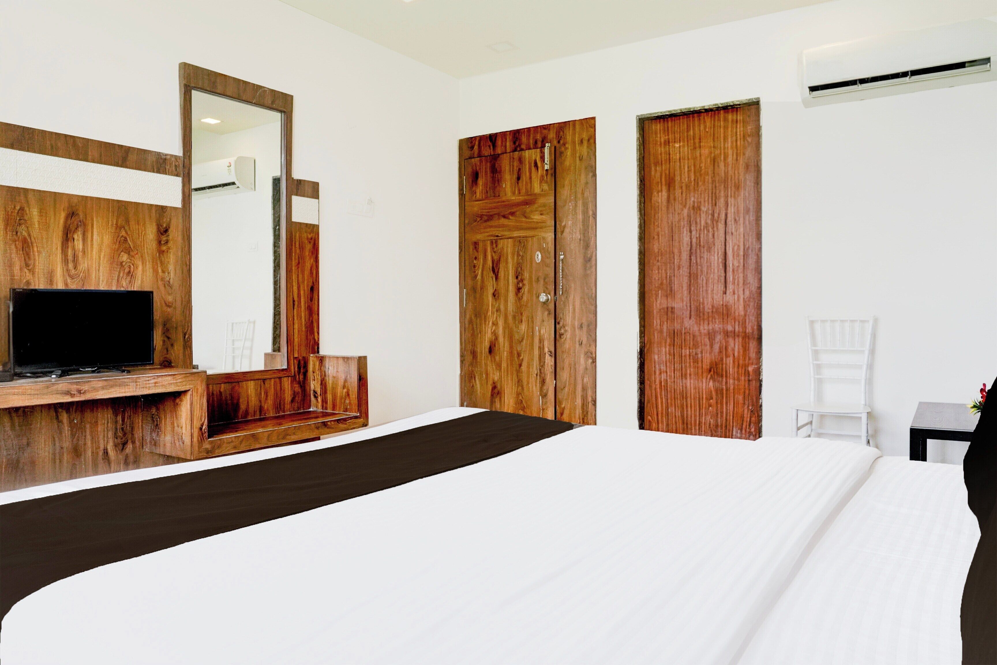 A hotel room with a large bed, a wooden desk, a television, and a wardrobe.