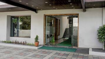A building entrance with a glass door, a small potted plant, a green mat, and a tiled pavement.