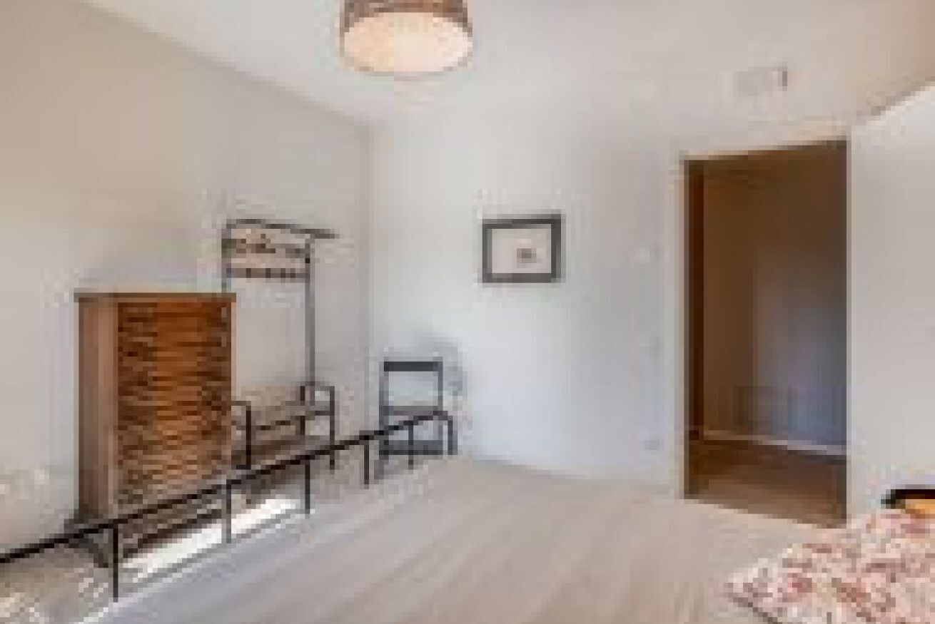 Ein Zimmer mit einem Holzkabinett, einem Stuhl, einem Bett und einer Tür zu einem anderen Raum.