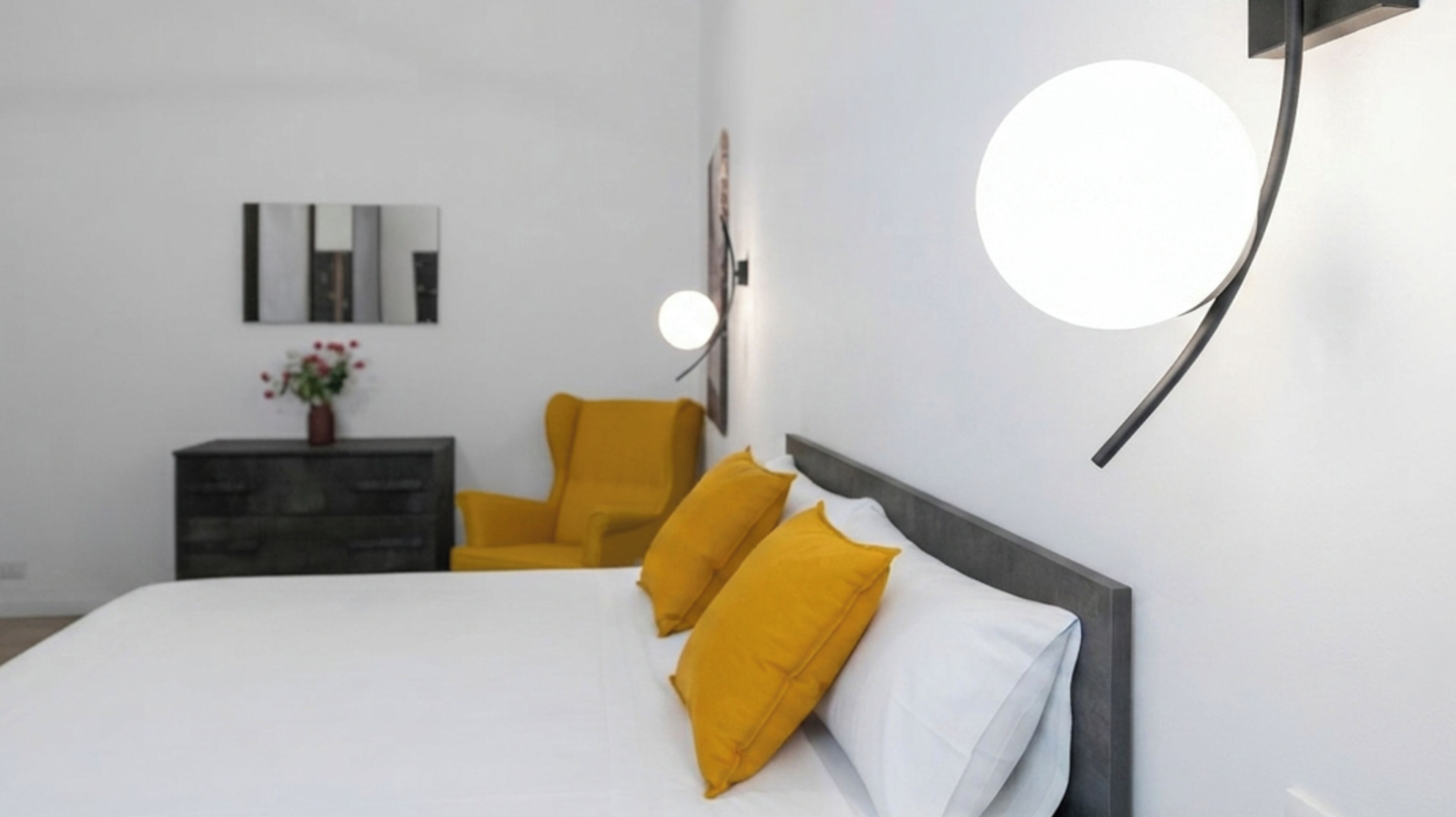 A modern bedroom with a bed, a nightstand, a chair, and a wall-mounted light fixture.