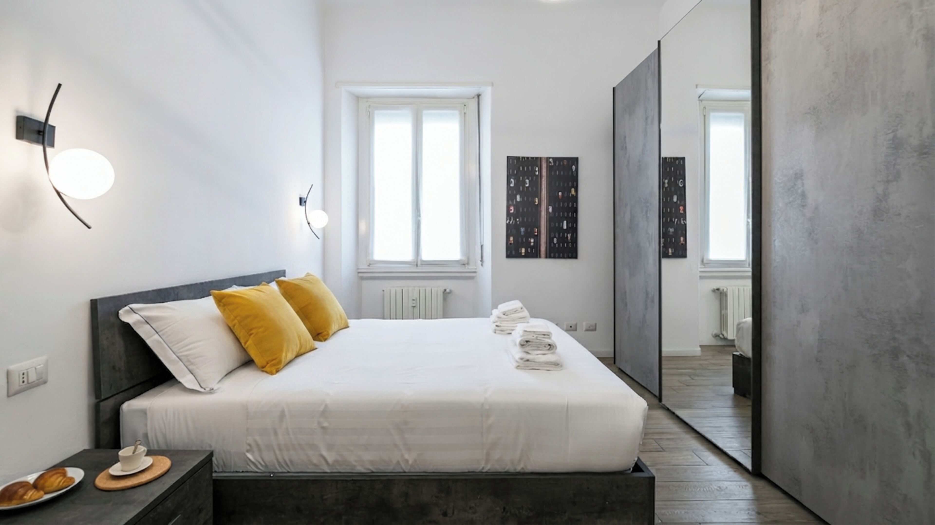 A modern bedroom with a bed, bedside table, and a view into another room.
