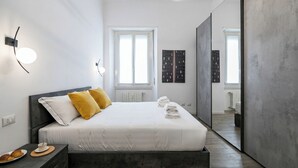 A modern bedroom with a bed, bedside table, and a view into another room. - Italianway Comfort - Cellini 1 (Milan)