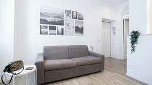 A living room with a grey sofa, a small table with a zebra-patterned bag, and a wall with multiple framed pictures. - Italianway Comfort - Cellini 1 (Milan)