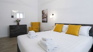 Een hotelkamer met een bed, een stoel, een dressoir en een lampje aan de muur.