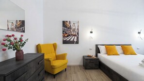 A hotel room with a bed, a chair, a dresser, a nightstand, and two wall-mounted lights. - Italianway Comfort - Cellini 1 (Milan)