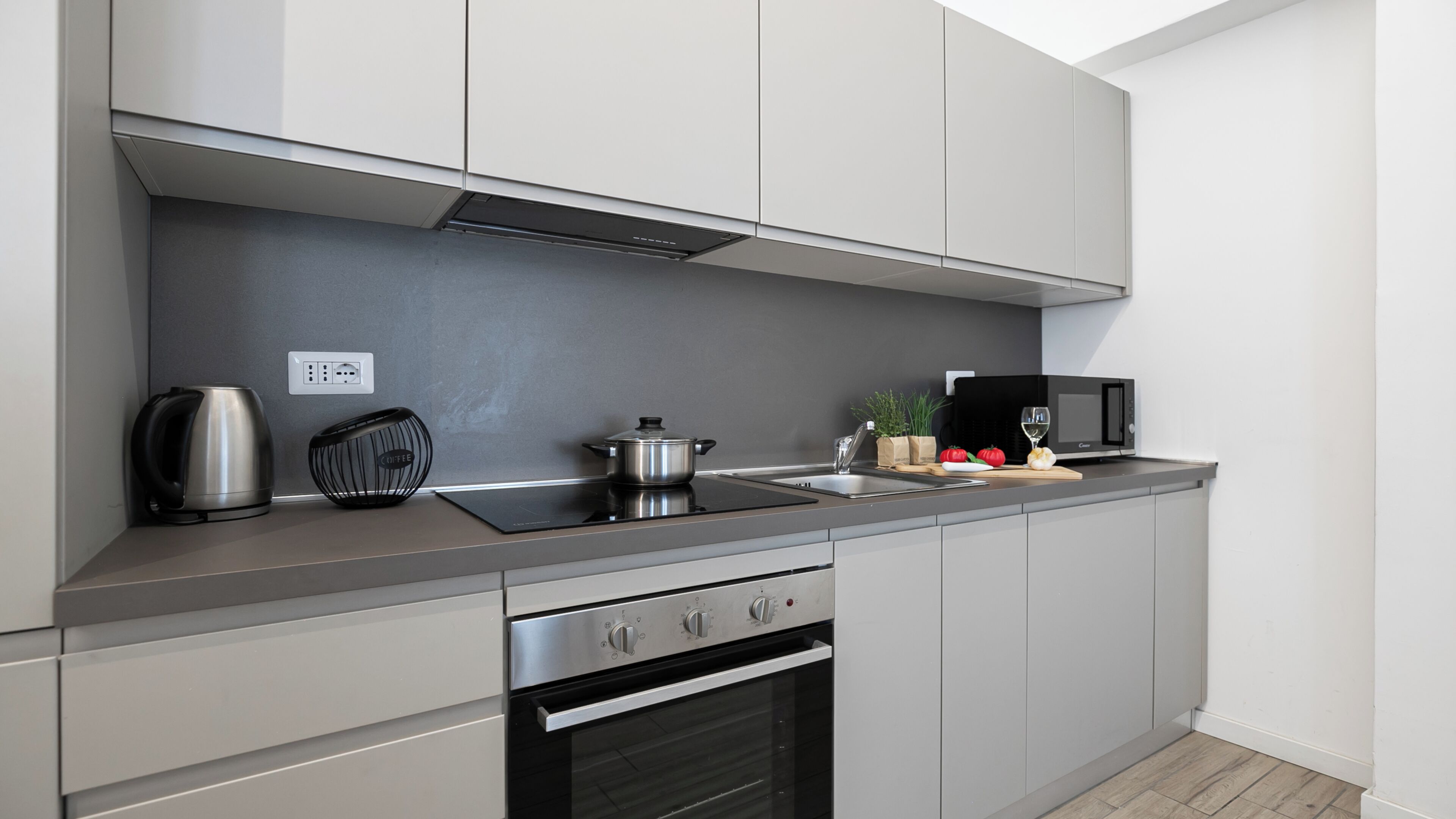 Een moderne keuken met een ingebouwde oven, een koffiezetapparaat, een magnetron en een pan op het aanrecht.