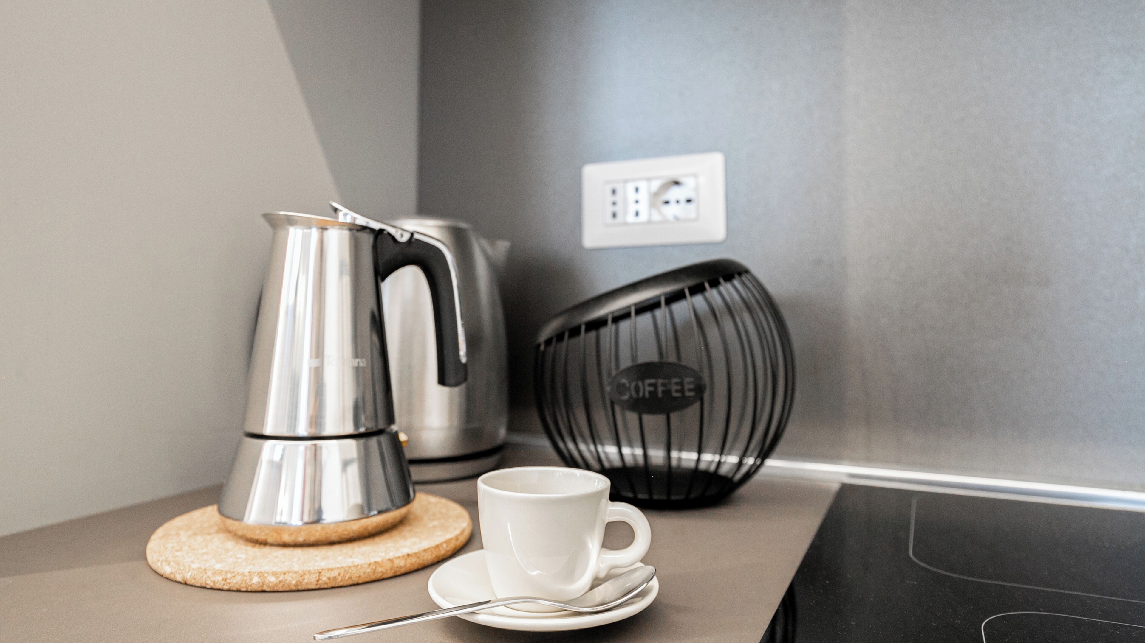 A kitchenette with a coffee maker, a cup, and a coffee grinder on a countertop.