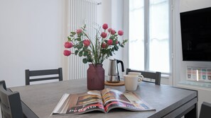 A dining table with a magazine, a vase with flowers, and a coffee pot. - Italianway Comfort - Cellini 1 (Milan)