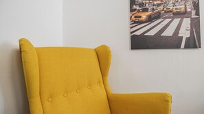 Een gele fauteuil tegen een witte muur met een stadslandschap schilderij.