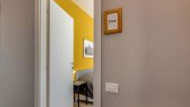 A hallway with a door leading to a room, a framed picture on the wall, and a chair in the background. - GuestHost - Family & Friends House - Stanza Travel (Padua)