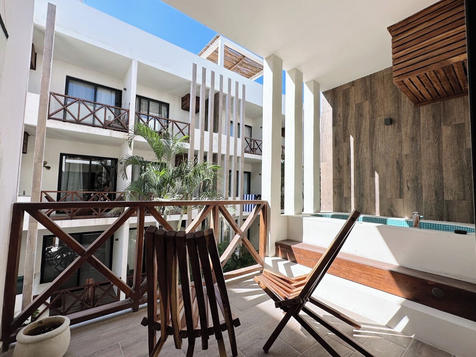 Un balcon avec une chaise en bois, une plante et un espace piscine.