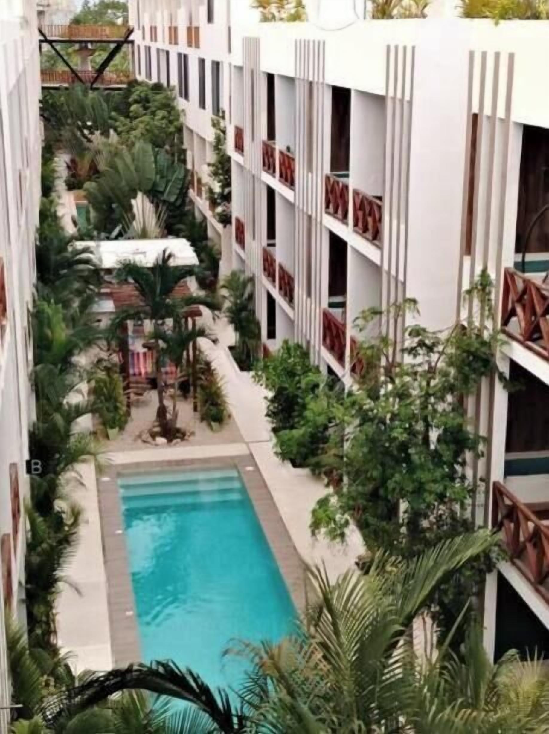 A multi-story hotel with a central pool surrounded by lush greenery and balconies.