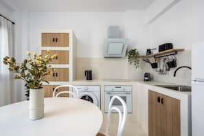 A modern kitchen with wooden cabinets, a built-in oven, a washing machine, and a dining area with a table and chairs. - Villa located in Lindos (Rhodes)