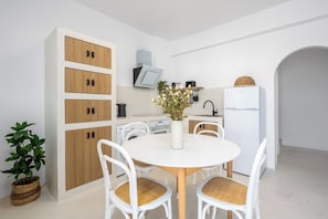 A modern kitchen with white cabinets, a dining table with chairs, and a small potted plant. - Villa located in Lindos (Rhodes)