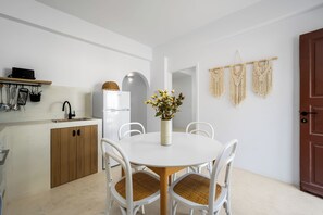 A modern kitchen with white cabinetry, a built-in oven, and a sink. There is a dining table with four chairs and a vase with flowers. - Villa located in Lindos (Rhodes)