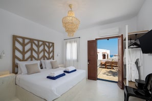A bedroom with a bed, a chandelier, a wooden headboard, a door leading to a balcony, and a view of the sea. - Villa located in Lindos (Rhodes)