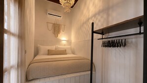 A bedroom with a bed, an air conditioning unit, a hanging macrame decoration, and a coat rack with hangers. - Villa located in Lindos (Rhodes)