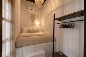 Quarto com cama, ar condicionado, decoração de macramé pendente e cabideiro com ganchos.
